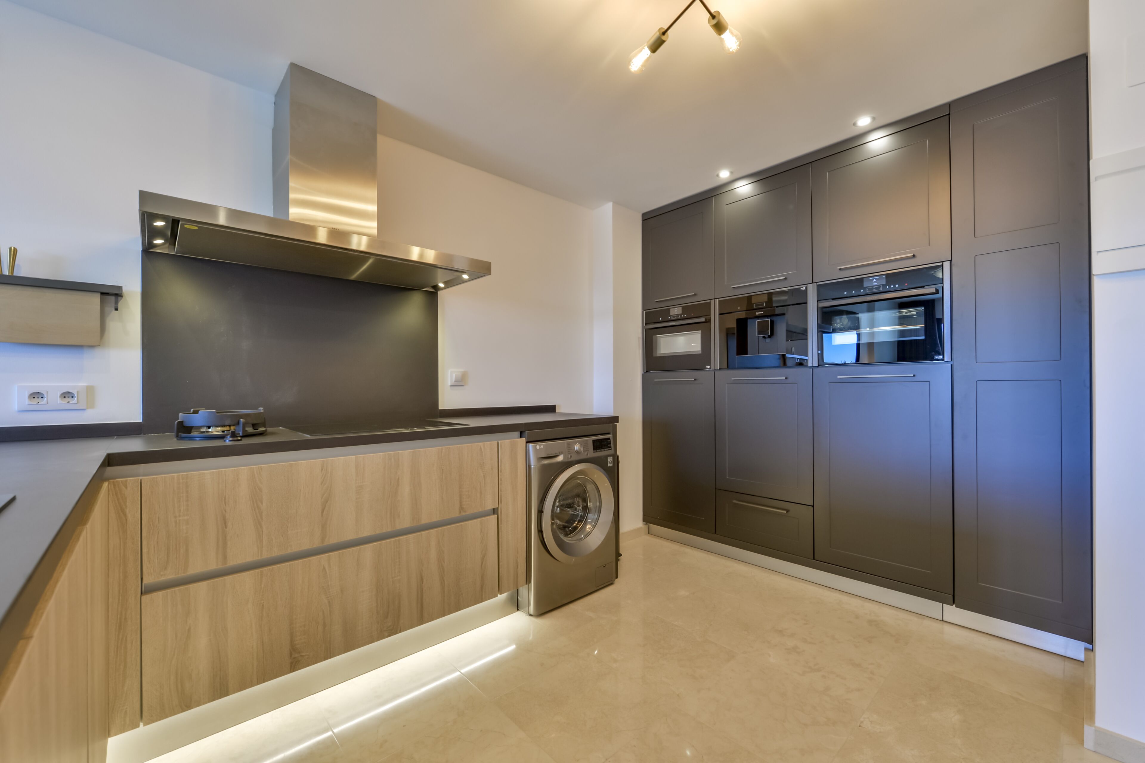 Une cuisine moderne dotée d’un lave-linge encastré, d’appareils électroménagers en acier inoxydable et de meubles de rangement en bois.