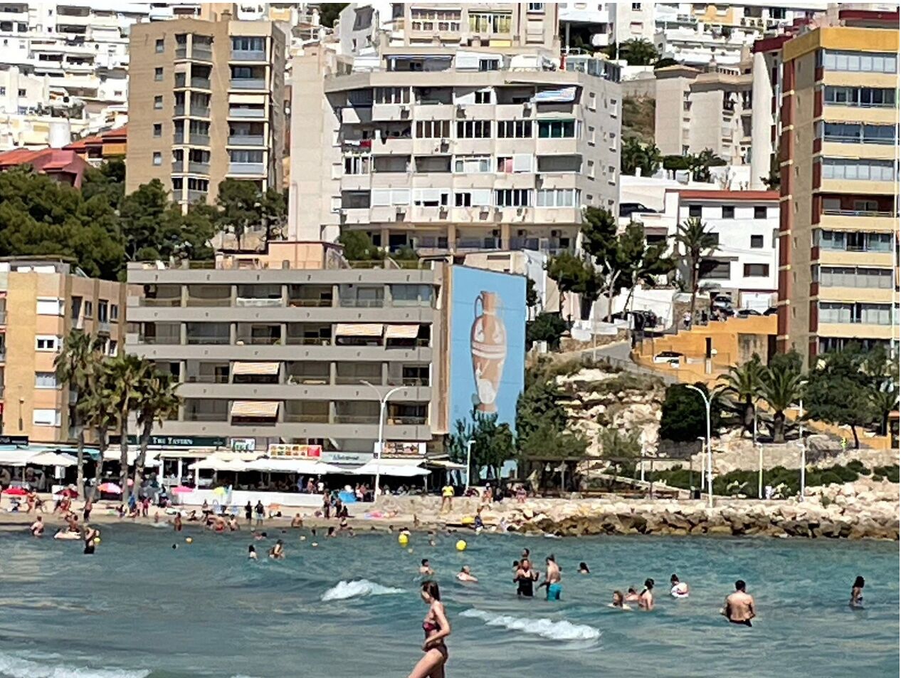 Eine Küstenstadt mit Strand, badenden Menschen und einem großen Gebäude mit Wandgemälde.