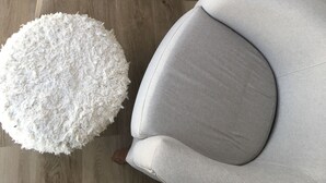 Ein modernes Wohnzimmer mit einem grauen Sessel, einem weißen runden Couchtisch und einem flauschigen weißen Pouf.