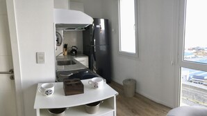 Eine kleine Küche mit Spüle, einem schwarzen Kühlschrank und einem Fenster mit Blick nach draußen.