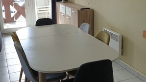 A dining area with a large table, chairs, a cabinet, a TV, and a window with curtains. - APARTMENT IN MORBIHAN - DIRECT ACCESS TO THE PORT AND BEACH ON FOOT (Arzon)