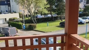A balcony with a tiled floor and a view of parked cars and buildings in the background. - APARTMENT IN MORBIHAN - DIRECT ACCESS TO THE PORT AND BEACH ON FOOT (Arzon)