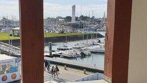 A view from a balcony overlooking a marina with boats docked, a tower in the background, and a sign for 'La Presqu'ille'. - APARTMENT IN MORBIHAN - DIRECT ACCESS TO THE PORT AND BEACH ON FOOT (Arzon)