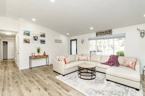 Relax in this inviting living space with a large L-shaped sofa, coffee table, and console table, offering a view of lush greenery outside.