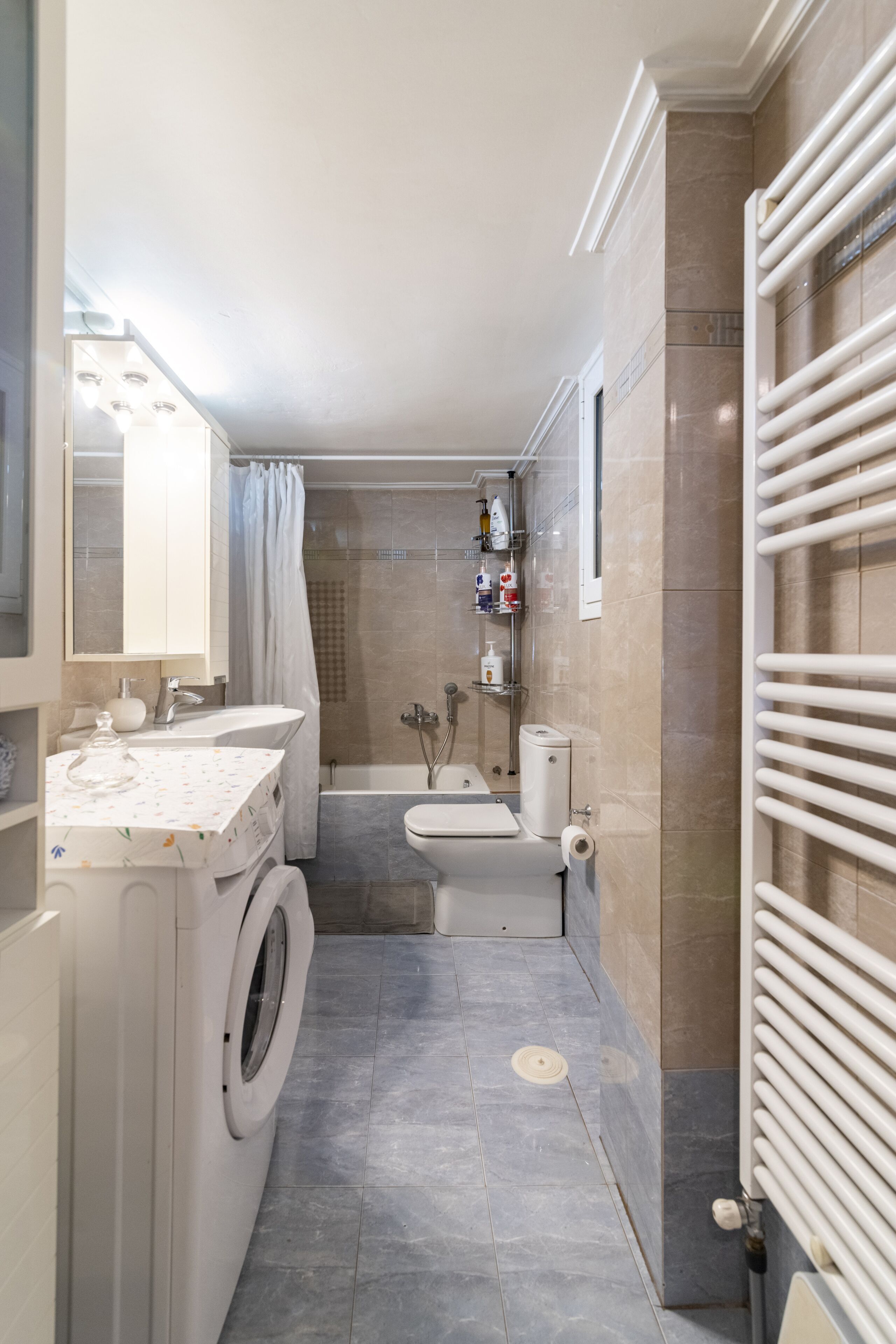 Een kleine badkamer met een wasmachine, wastafel, bad en toilet.