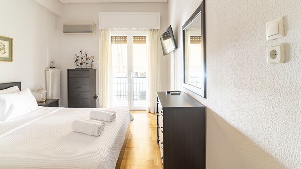 Una habitación de hotel con cama, cómoda, televisión y ventana con cortinas.