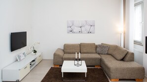 A modern living room with a sectional sofa, a flat-screen TV, a coffee table, and a decorative wall piece. - Bright, chic apartment in the heart of Düsseldorf near the main train station (Düsseldorf)
