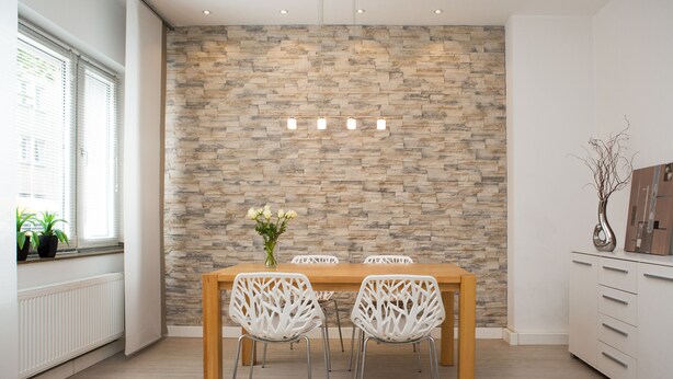 A dining area with a wooden table and white chairs, a stone wall, and a window with blinds. - Bright, chic apartment in the heart of Düsseldorf near the main train station (Düsseldorf)