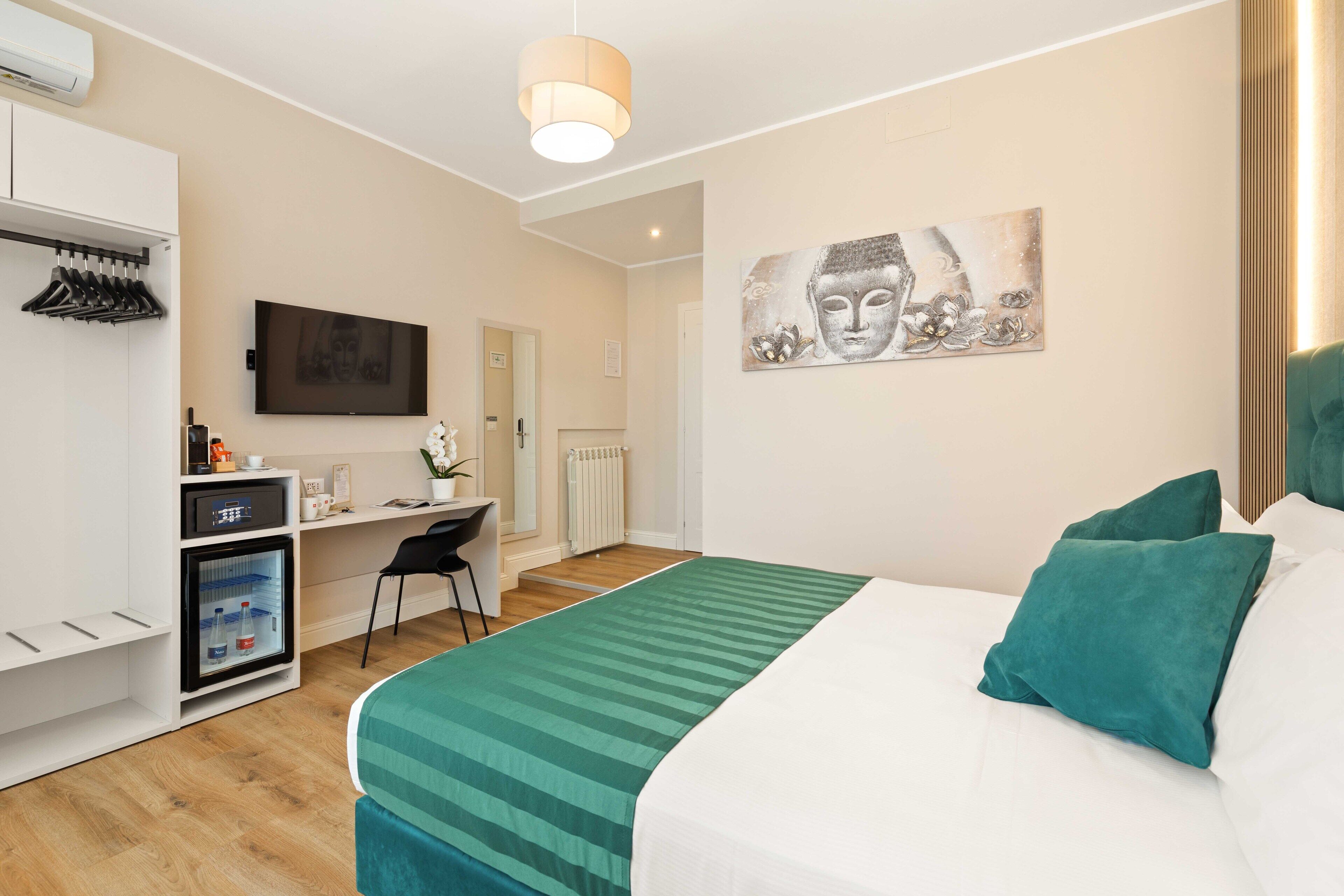 A hotel room with a bed, a desk, a chair, a wardrobe, a television, and a Buddha painting.