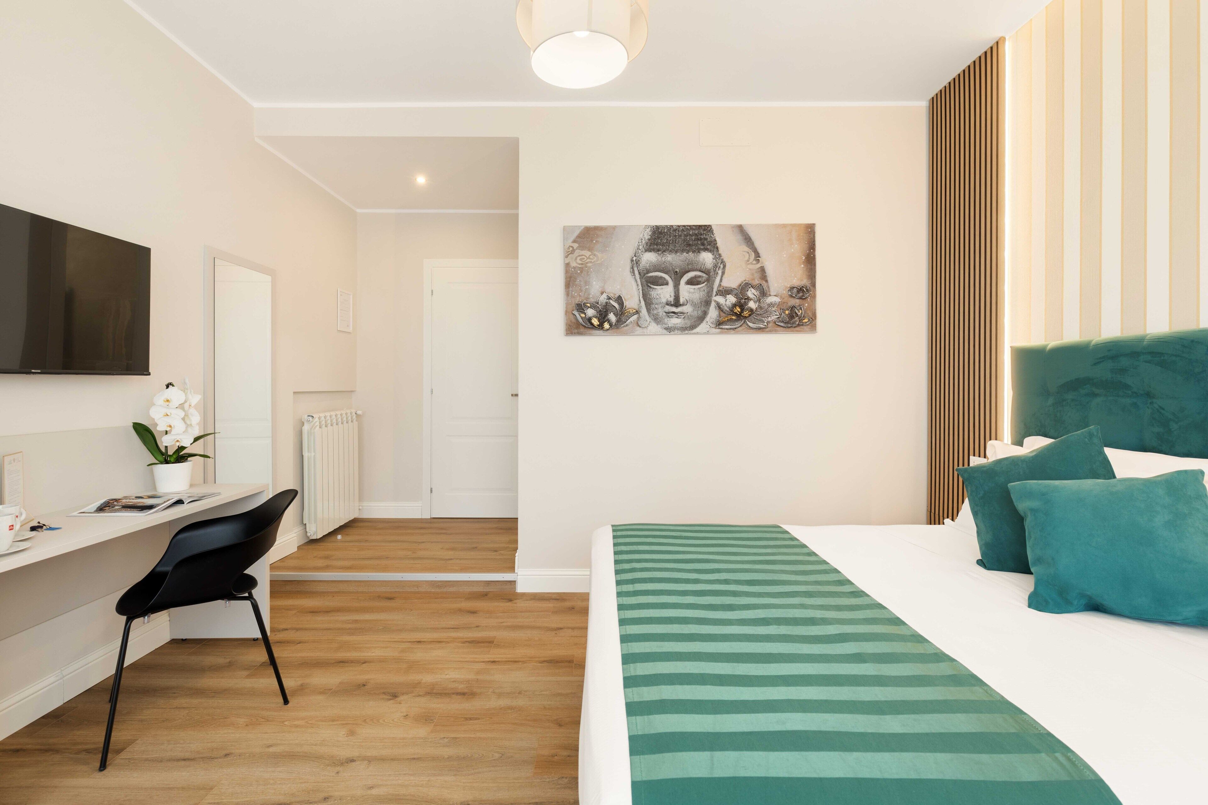 A modern hotel room with a bed, a desk, and a large Buddha painting on the wall.