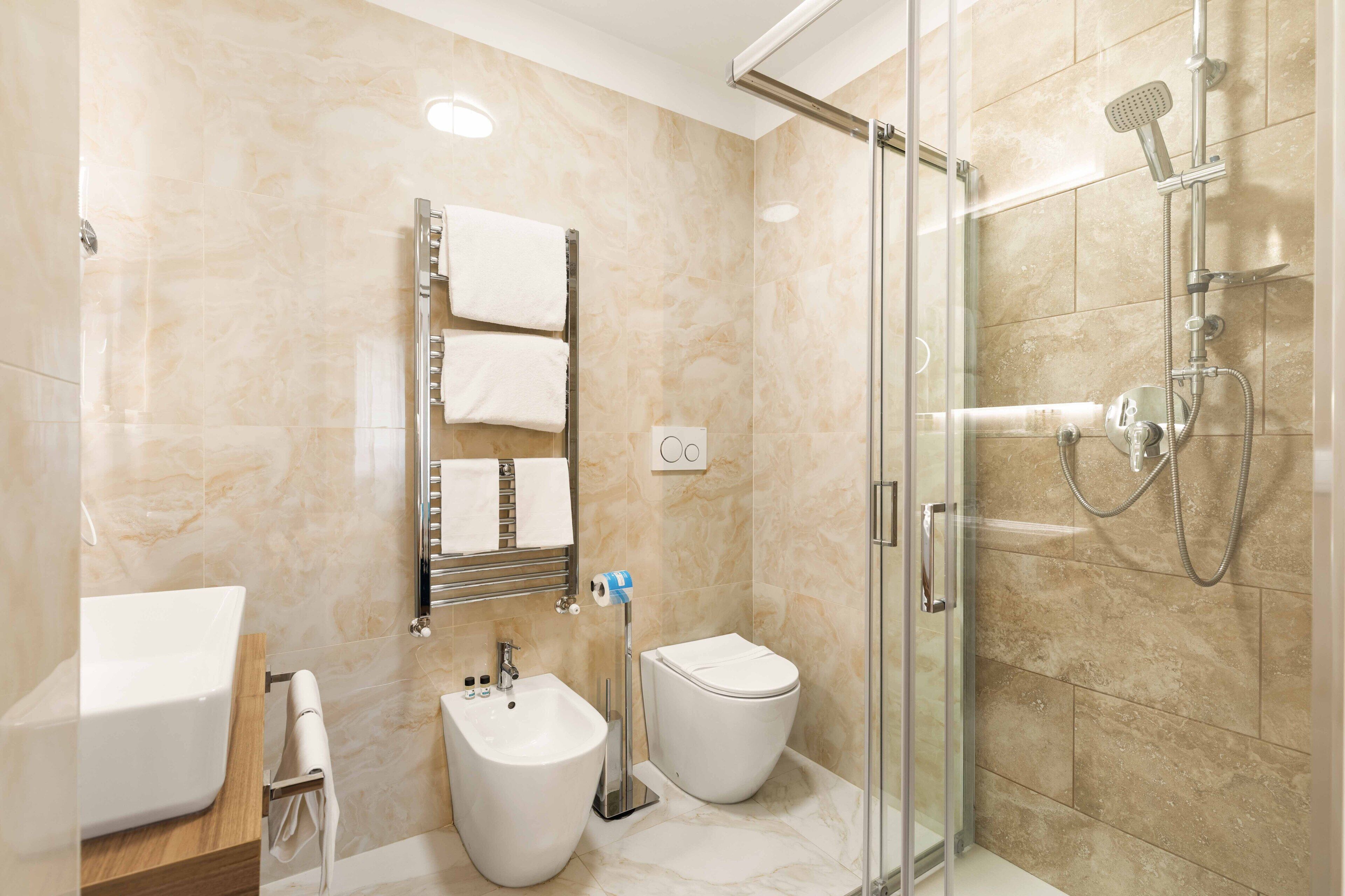 A modern bathroom with a glass-enclosed shower, a bidet, a toilet, and a sink.