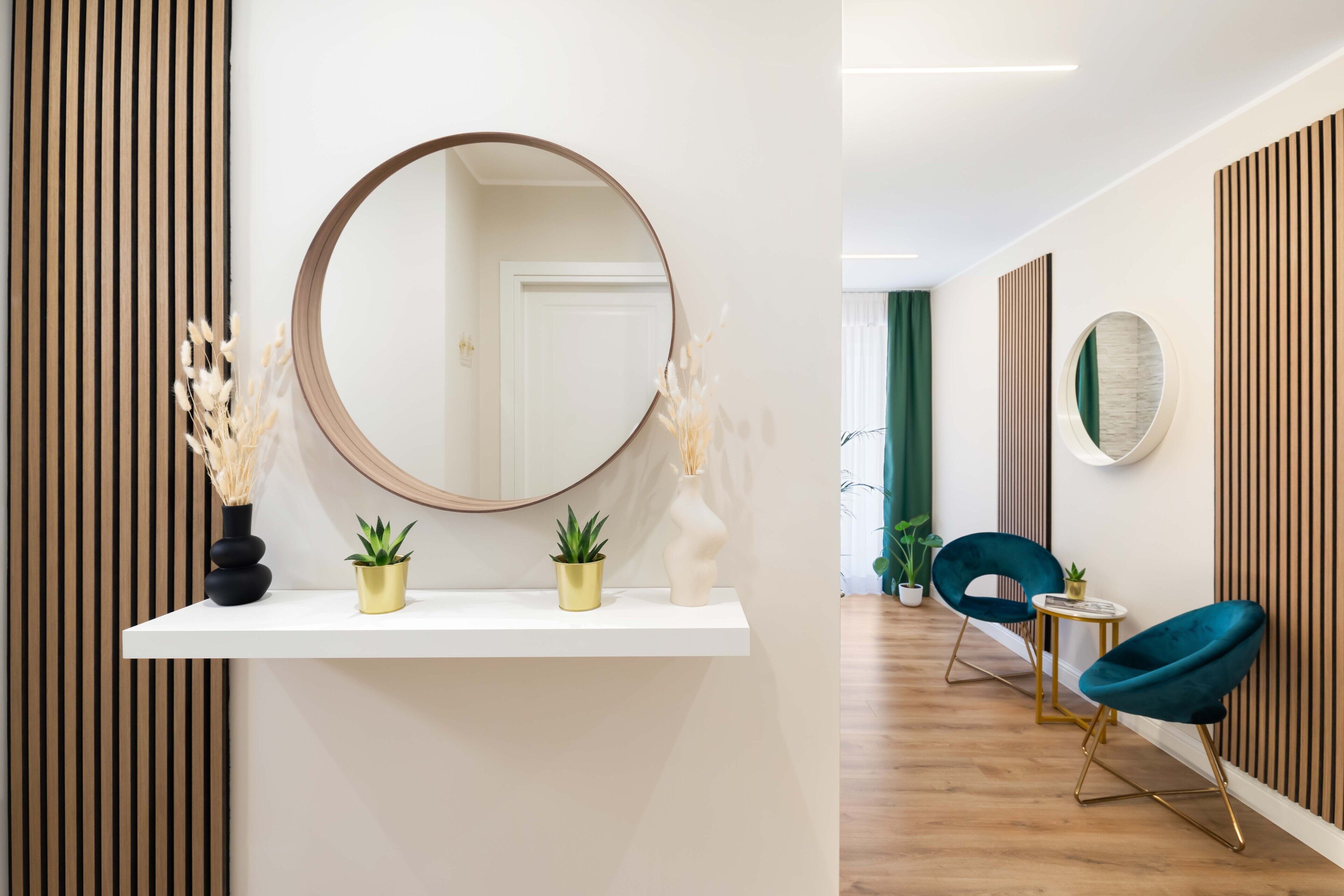 A modern interior with a white shelf holding three potted plants, a large round mirror, and a wooden slat wall.