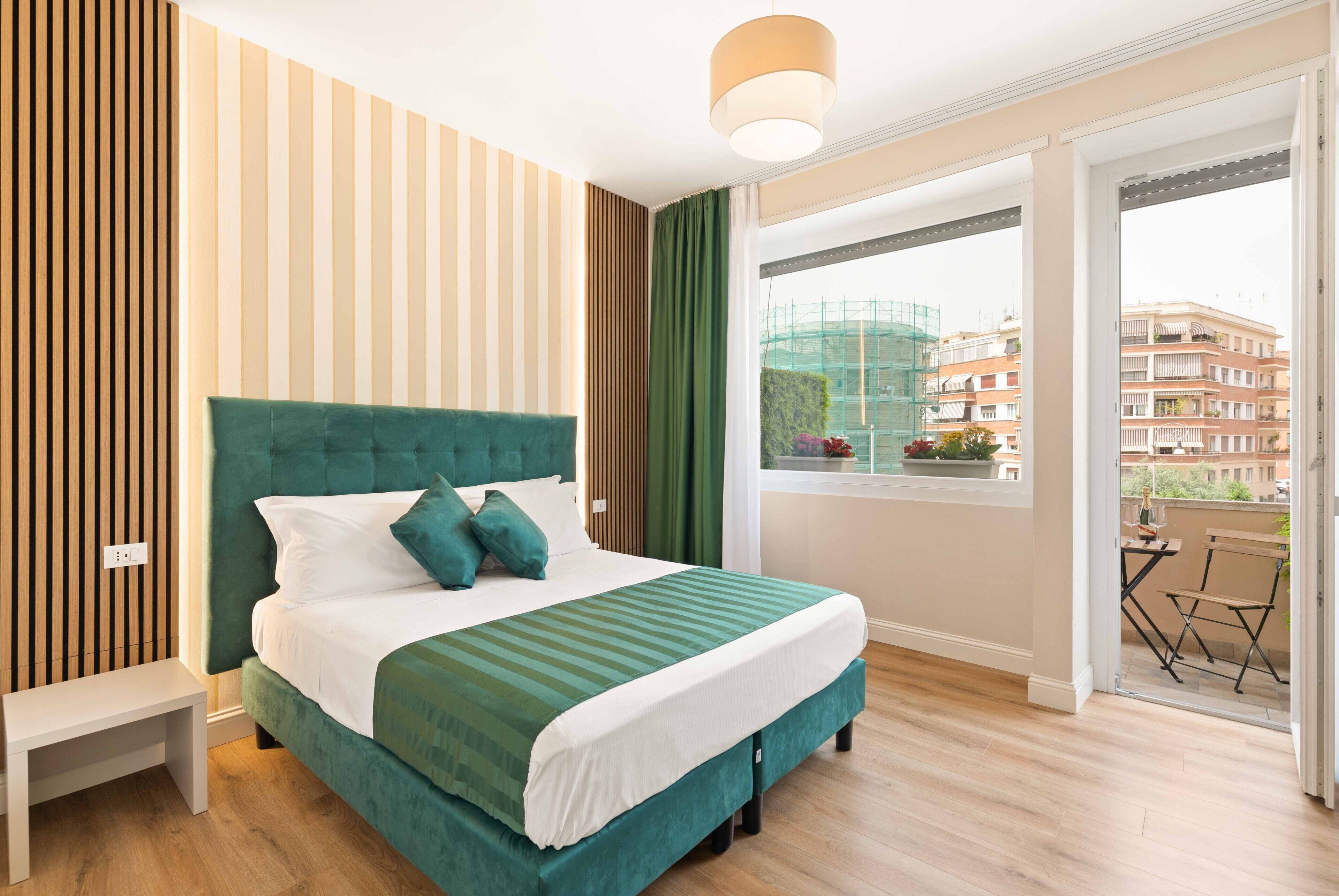 A modern bedroom with a large bed, a bench, and a view of the city through a balcony.