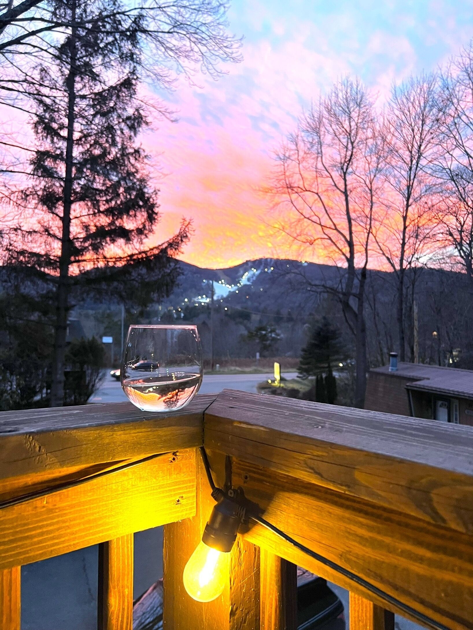 Ein Glas Weißwein auf einer Holzterrasse, über dem hängt eine Glühbirne.