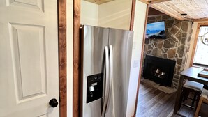 A modern kitchen with a stainless steel refrigerator, a stone fireplace, and wooden ceiling beams. - Dog-Friendly Banner Elk Condo w/ Slope View and Deck (Banner Elk)