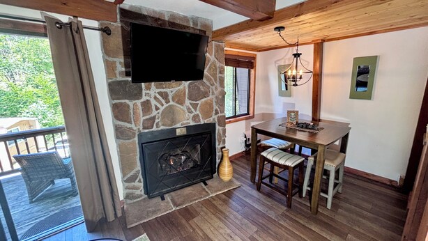 A cozy room with a stone fireplace, wooden ceiling beams, a dining table with chairs, and a TV mounted on the wall. - Dog-Friendly Banner Elk Condo w/ Slope View and Deck (Banner Elk)