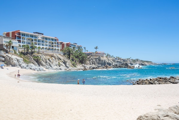 A beachfront hotel with multiple balconies, a rocky shoreline, and clear blue waters.