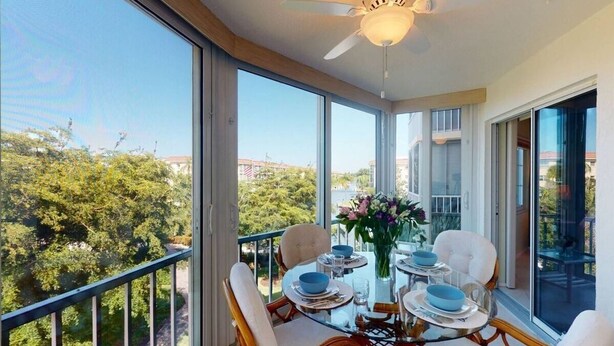 Een balkon met een eettafel, grote ramen en een plafondventilator.