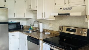A modern kitchen with white cabinets, granite countertops, stainless steel appliances, and a black stove. - Beautiful Wells Maine Premium Top Floor Condo at Village By The Sea 2 Bed 2 Bath (Wells)