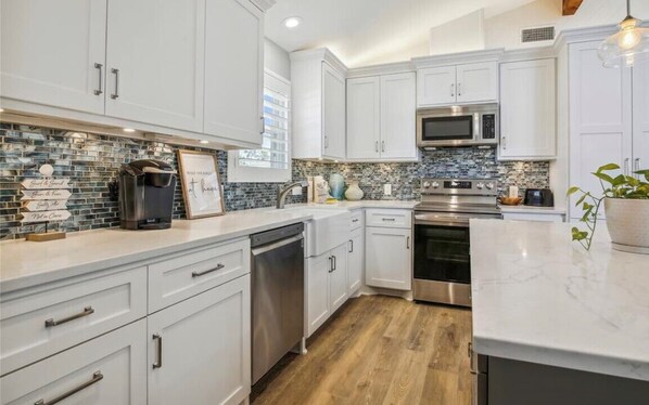 Enjoy cooking in this well-equipped kitchen with stainless steel appliances, a sink, and a countertop with a vase and a plant.