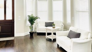 Una sala de estar con un sofá blanco, un sillón blanco, una mesita con una planta y un ventilador de techo.