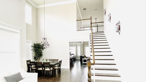 Amplia sala de estar con un sofá blanco, una mesa de comedor con sillas, una escalera de madera y una planta colgante.