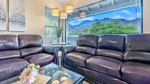 Ein Wohnzimmer mit einer Ledersofa, einem Glastisch und Blick auf Berge durch ein großes Fenster.