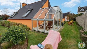 A house with a glass conservatory, a lawn, and a pink towel on a chair. - Les Bancs Roux - Binic Etables SUR MER (BINIC ETABLES SUR MER)