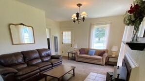 A spacious living room with a brown leather sofa, a beige sofa, and a coffee table. There is a fireplace with a mantel and a vase of flowers.