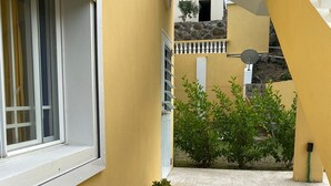 A yellow building with a window, a small planter with plants, and a tiled patio area. - Cozy Studio Apartment in Quiet Neighborhood (Philipsburg)