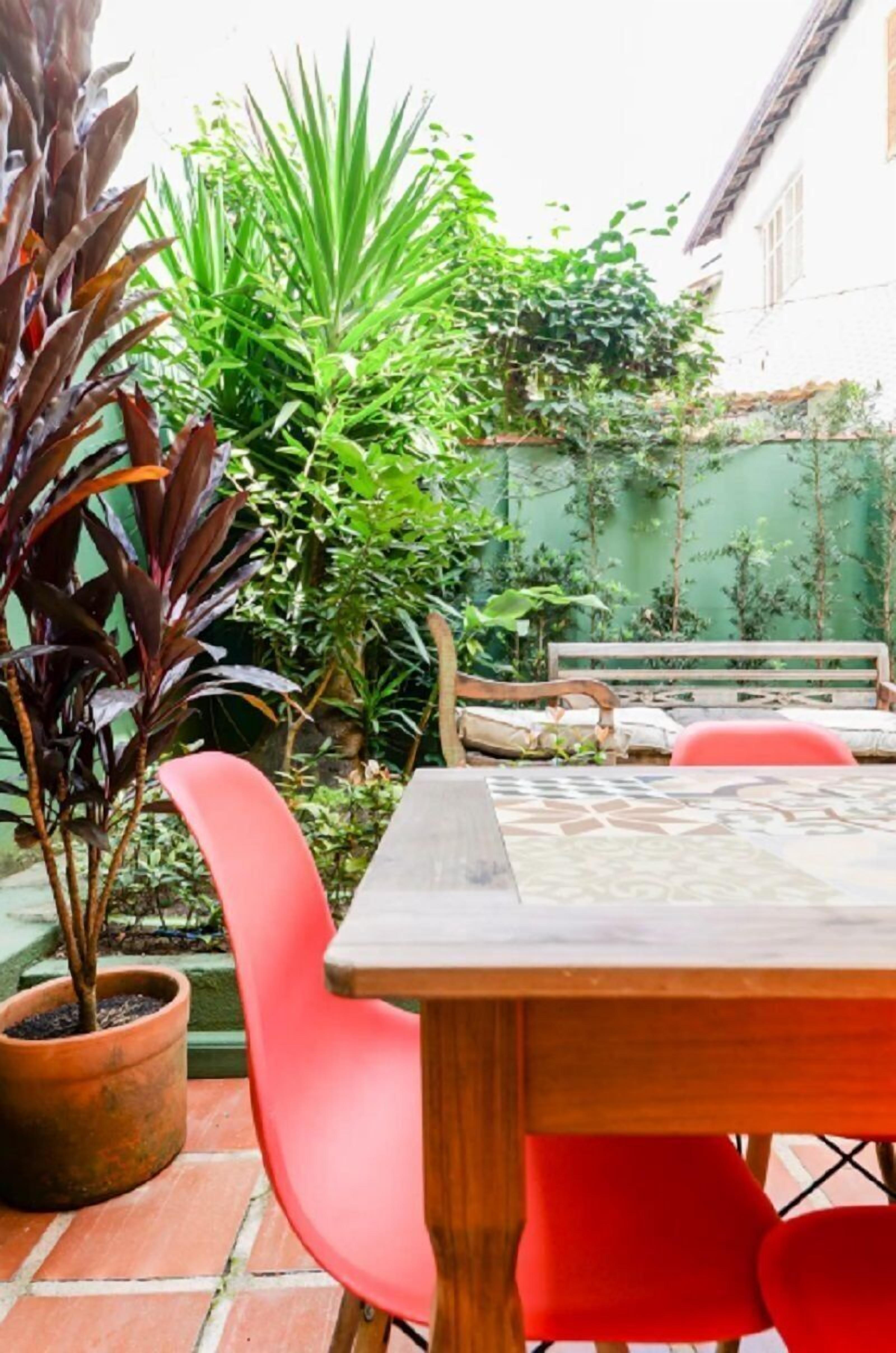Eine Terrasse mit einem Holztisch und roten Stühlen, umgeben von Topfpflanzen und einer grünen Wand.