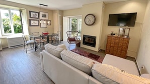 A spacious living room with a large sofa, a dining table with chairs, a fireplace, a television, and framed pictures on the wall. - Eighteen21 Houses - Casa da Mula in Quinta Velha (Sintra)