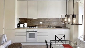 A modern kitchen with white cabinets, a wooden backsplash, a gas stove, and a hanging light fixture. - Eighteen21 Houses - Casa da Mula in Quinta Velha (Sintra)
