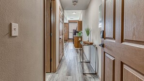 A hallway with wooden doors, a kitchen area with a brick backsplash, and a small table with a plant. - Deluxe Studio in Historic Downtown Building! (Bartlesville)