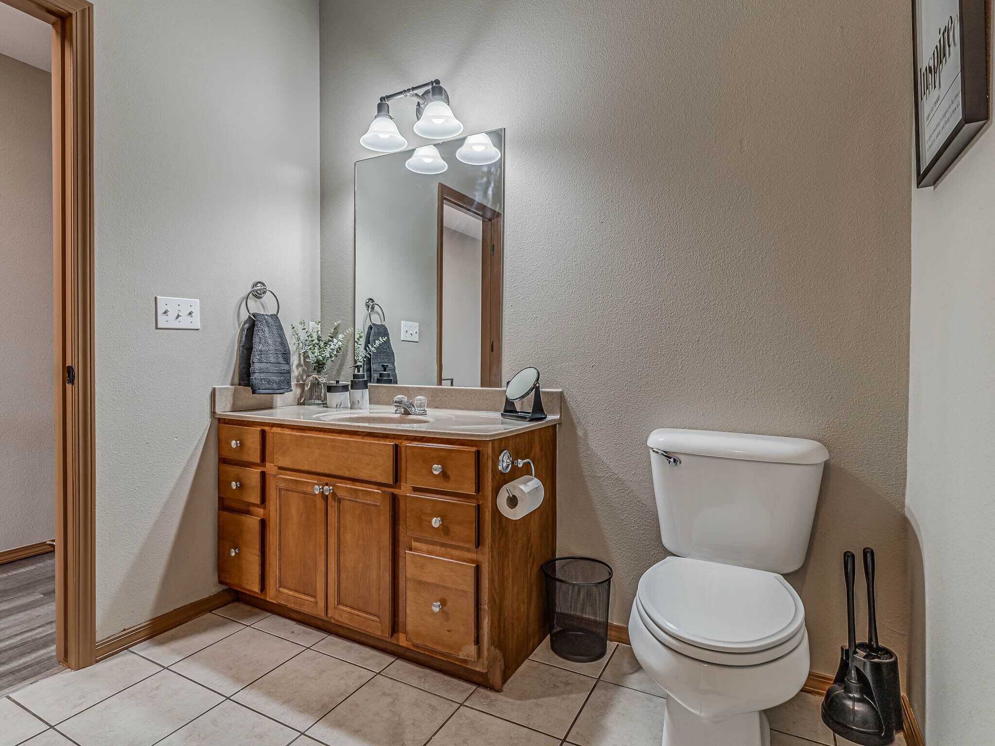 A bathroom with a wooden vanity, a mirror, a toilet, and a trash can.