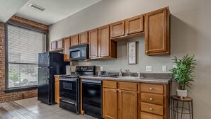 A kitchen with wooden cabinets, a black refrigerator, a microwave, a stove, and a sink. - Deluxe Studio in Historic Downtown Building! (Bartlesville)