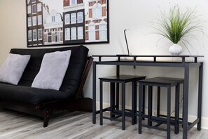 Ein modernes Wohnzimmer mit einer schwarzen Couch, zwei schwarzen Beistelltischen und einer weißen Vase mit Grünpflanzen.