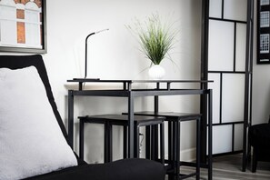 Una habitación moderna con un escritorio de metal negro, un florero blanco con plantas verdes y un cuadro en la pared.