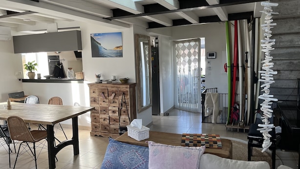 A modern living room with a wooden dining table, wicker chairs, and a large window. - RESIDENCE DE LA PLAGE (Bidart)