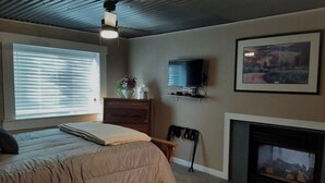 Quarto com cama, penteadeira, televisão, lareira e janela com persianas.