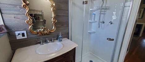 A bathroom with a white sink, a gold-framed mirror, a glass-enclosed shower, and wooden paneling on the wall.