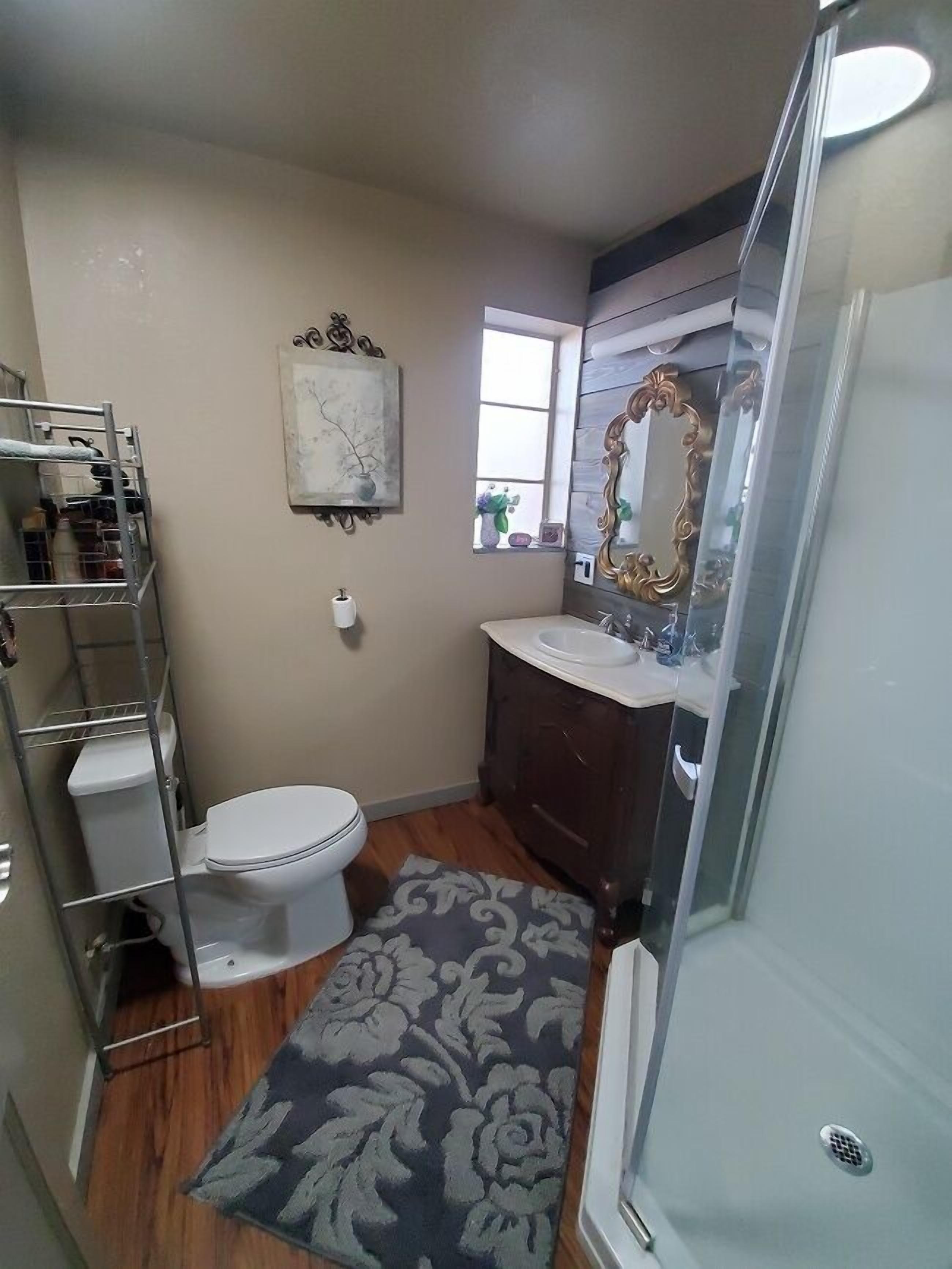 A compact bathroom with a toilet, a vanity with a mirror, and a shower area.