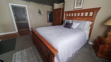 Quarto com cama de madeira, tapete cinza, guarda-roupa de madeira e uma porta.