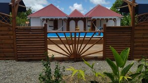 A gated area with a pool, wooden fences, and a building with a red roof. - Aïchi ´s Lodges (Capesterre-de-Marie-Galante)