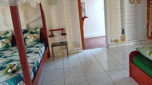 A room with a bed, a small table, a mirror, and a door leading to another room. - Aïchi ´s Lodges (Capesterre-de-Marie-Galante)