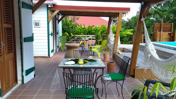 A covered patio area with a table and chairs, surrounded by potted plants and a hammock. - Aïchi ´s Lodges (Capesterre-de-Marie-Galante)