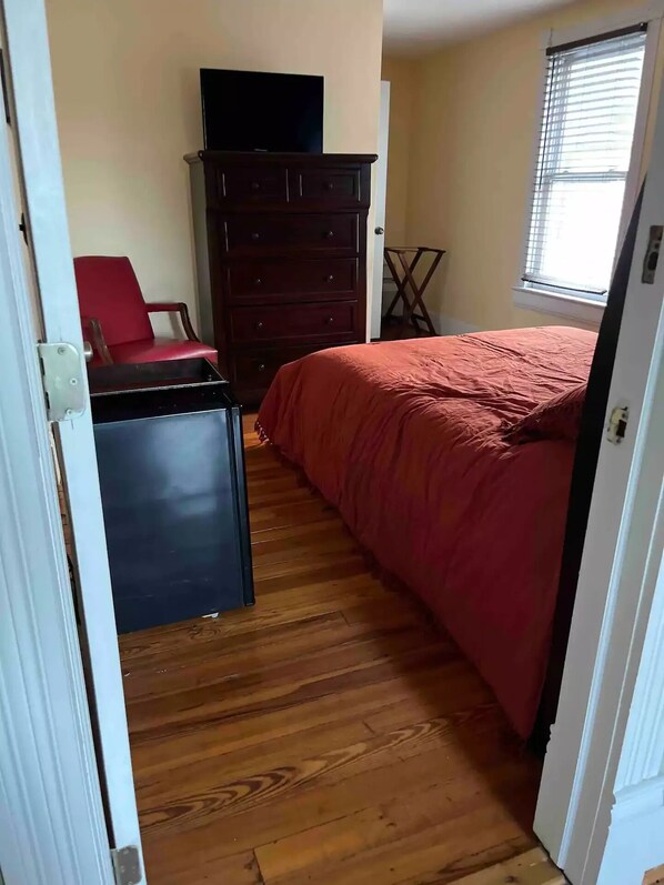 Cozy retreat with a comfortable bed, dresser, and TV, plus a window with blinds for natural light.