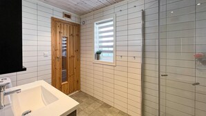 A bathroom with a wooden door, a window with blinds, a glass shower enclosure, and a white sink. - Amazing home in Sjusjøen with sauna (Sjusjøen)