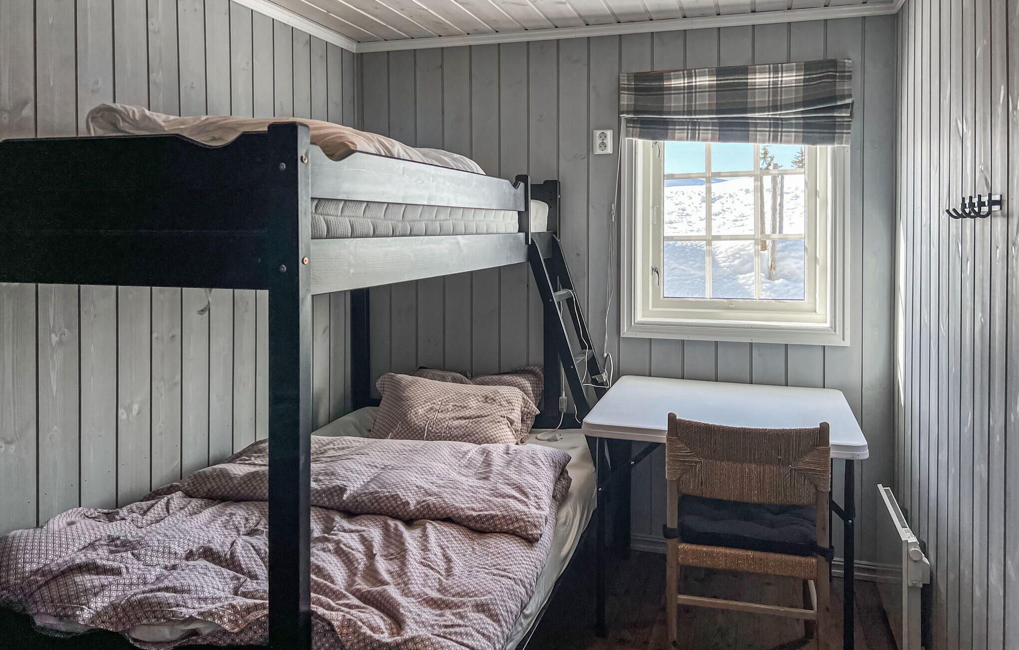 A bunk bed with a desk and chair, a window with a view of snow, and a radiator.