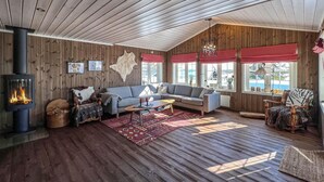 A cozy living room with a fireplace, wooden walls, a sofa, and a large window. - Amazing home in Sjusjøen with sauna (Sjusjøen)